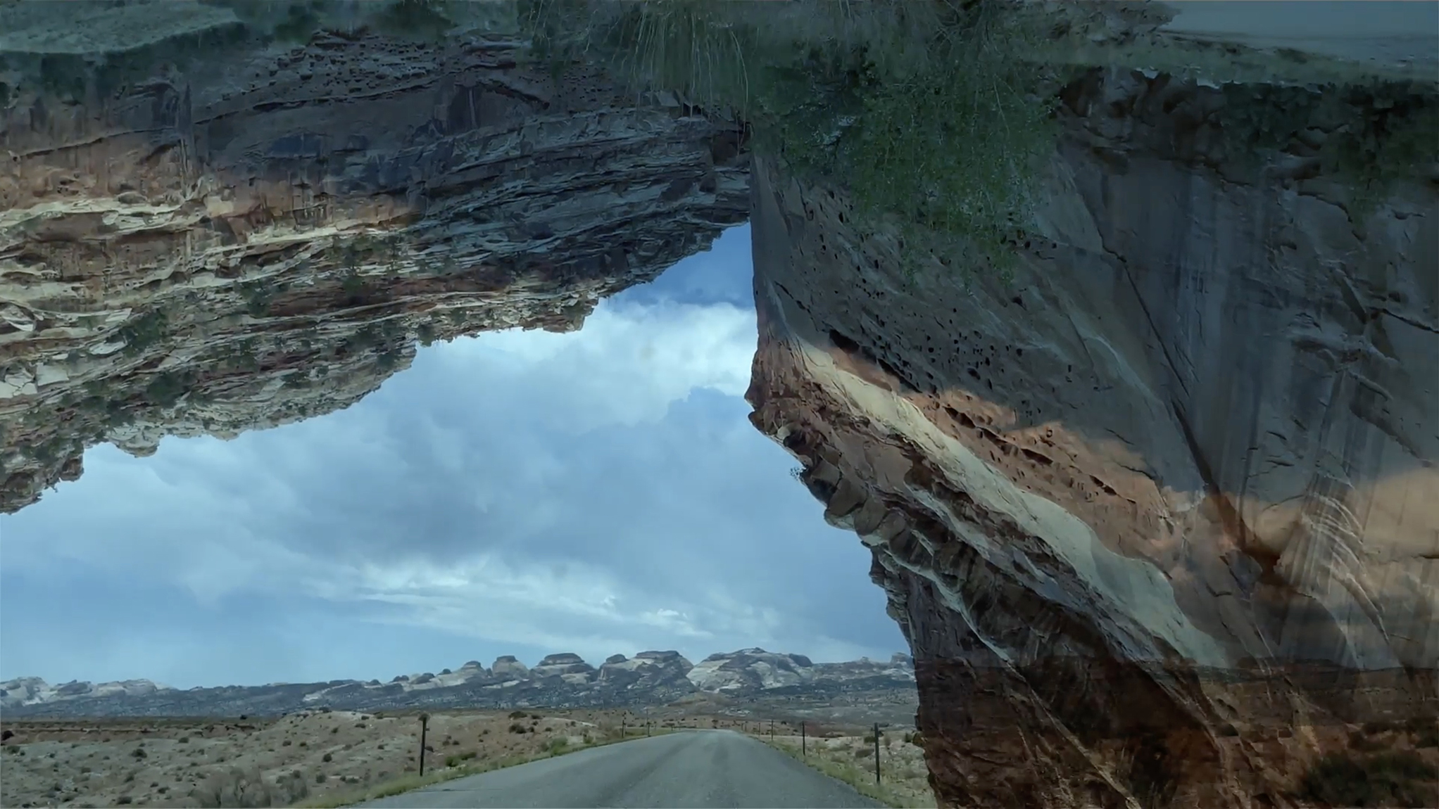 A still of a video of the middle of the road in the desert overlaid with an upside down overlay of mountains
