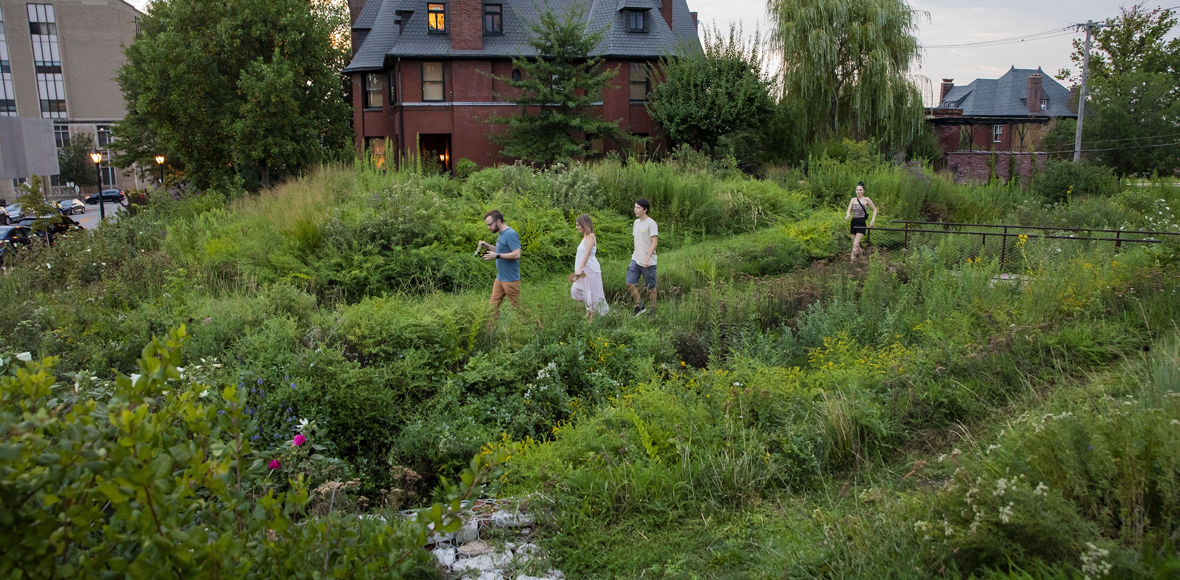 4 people walking across a grassy garden beside a brick house