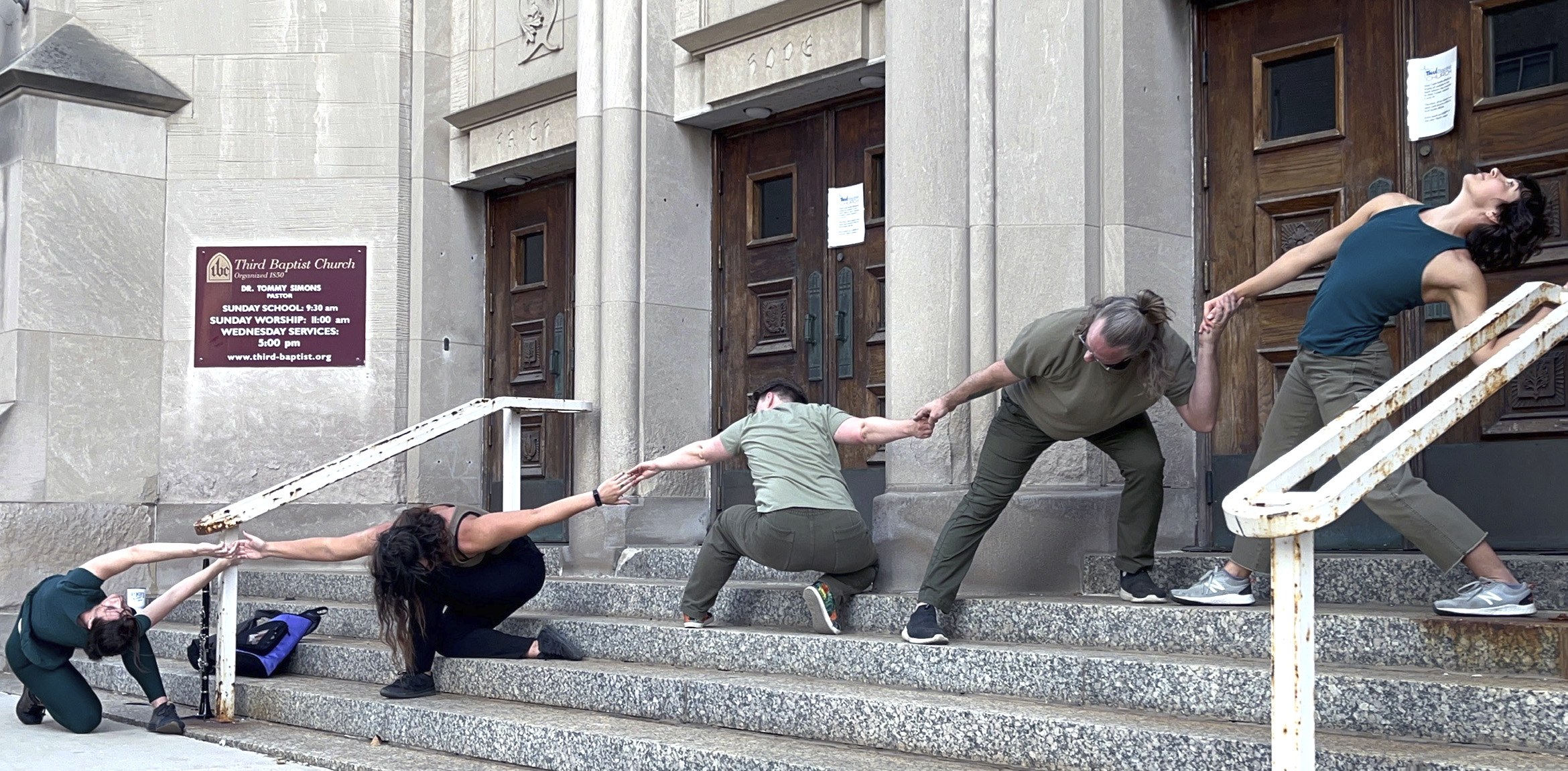 5 dancers on steps in front of a building in various poses linked together by holding hands