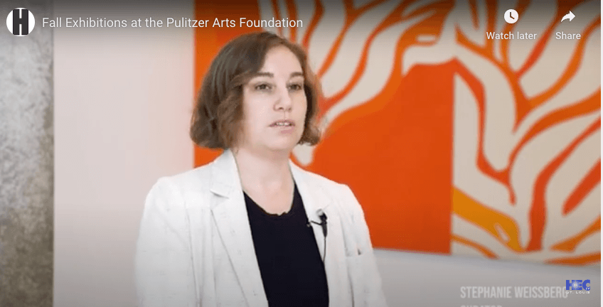 Video still of an interview with curator Stephanie Weissberg in front of a bright orange and white abstract painting