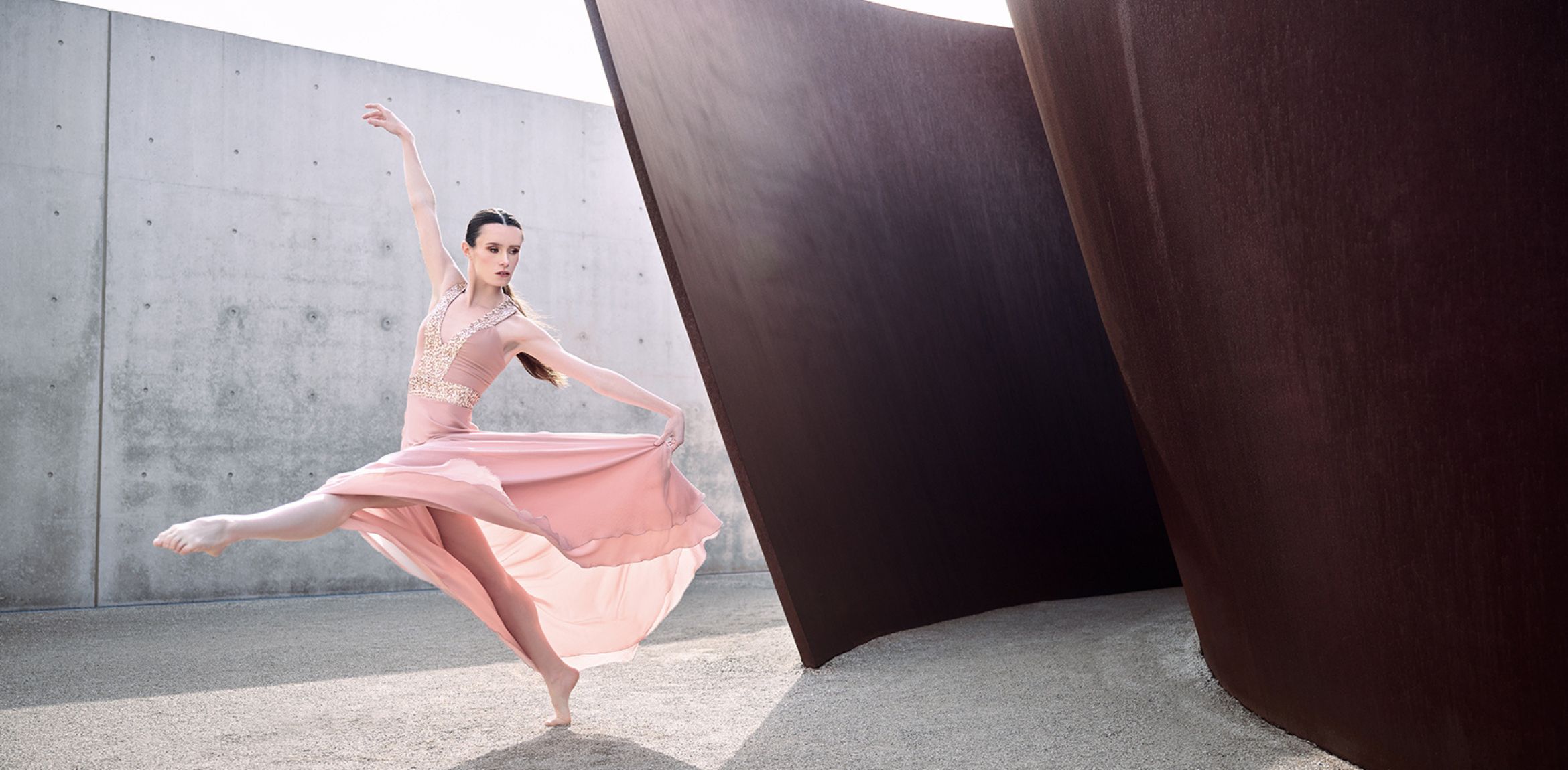 Dancer in flowy pink dress posing next to Richard Serra sculpture.