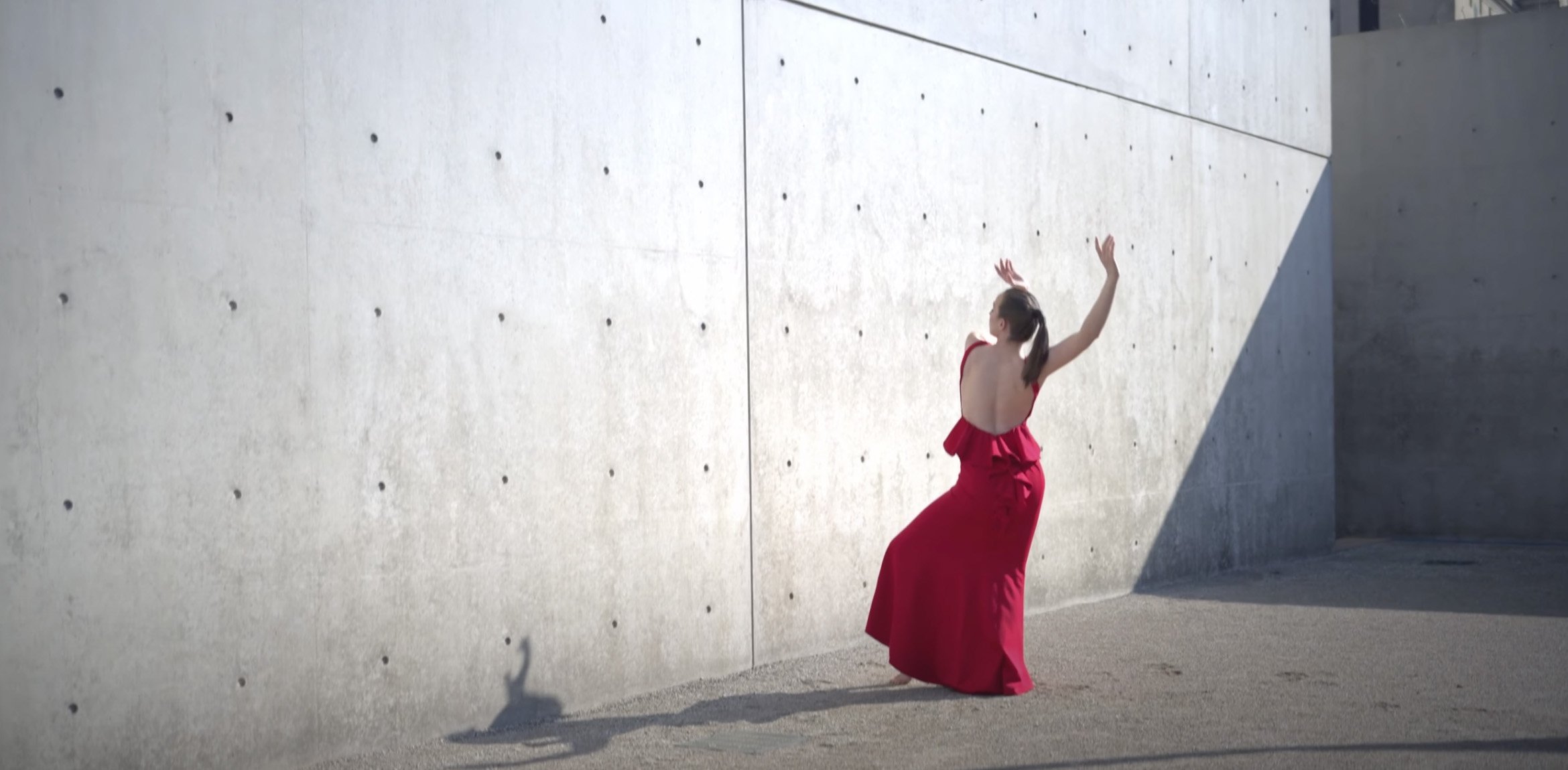 Dancer in a long red dress dancing in front of a concrete wall by the museum