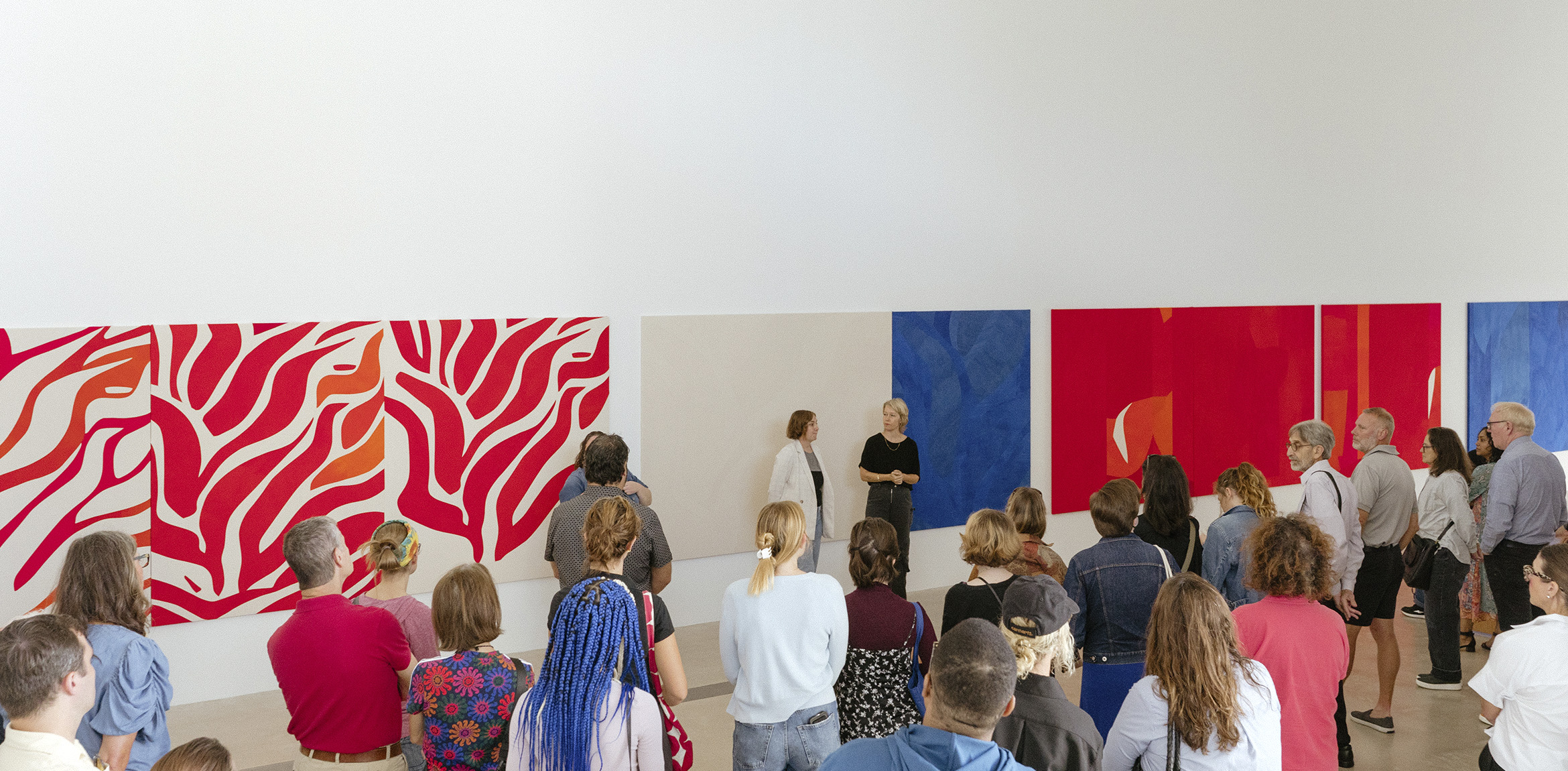Sarah Crowner and Stephanie Weissberg in front of two large crowner paintings while a crowd looks on
