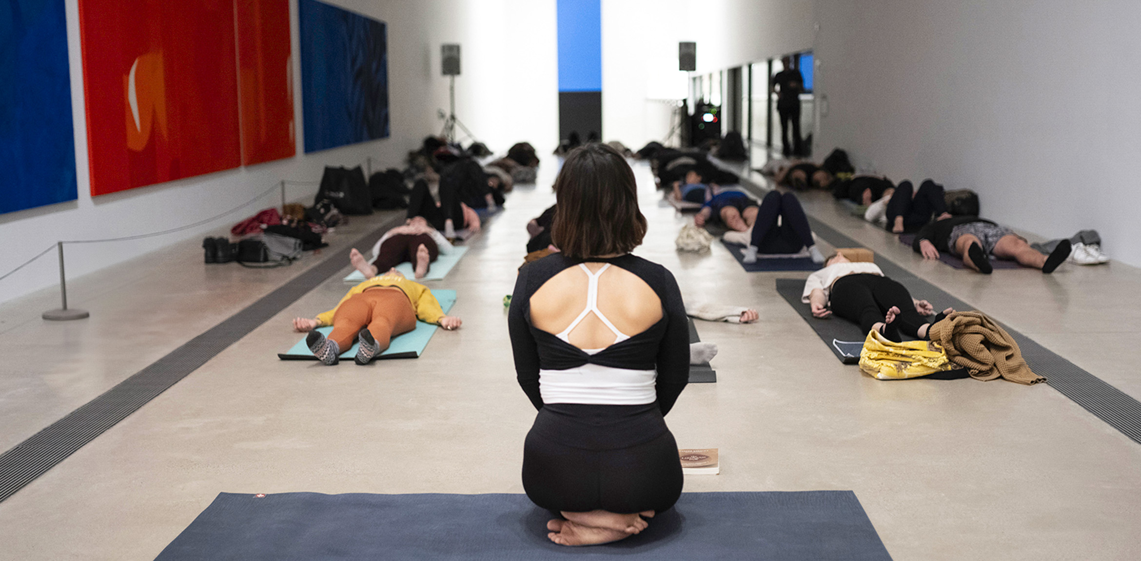 Back view of a yoga instructor with participants laying on the floor at the museum main gallery