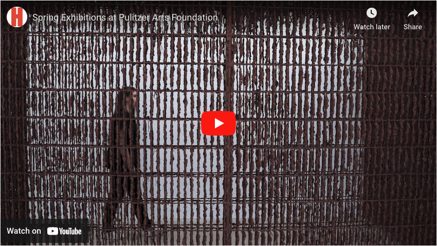 Video still of woman walking behind a mud covered fence, YouTube logo centers the still