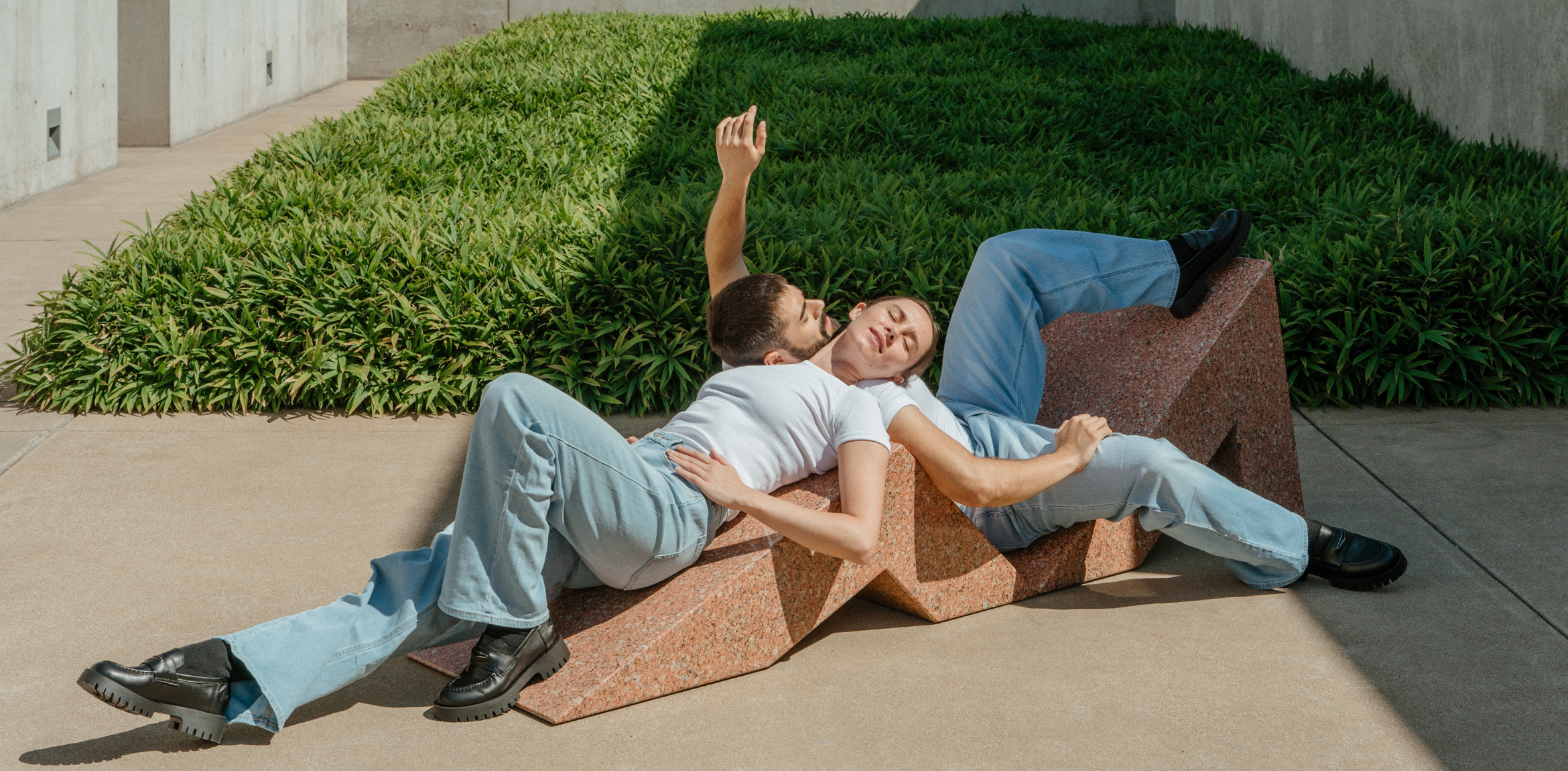 Two people laying with their bodies facing opposite on a granite chaise longue outside in the Pulitzer courtyard