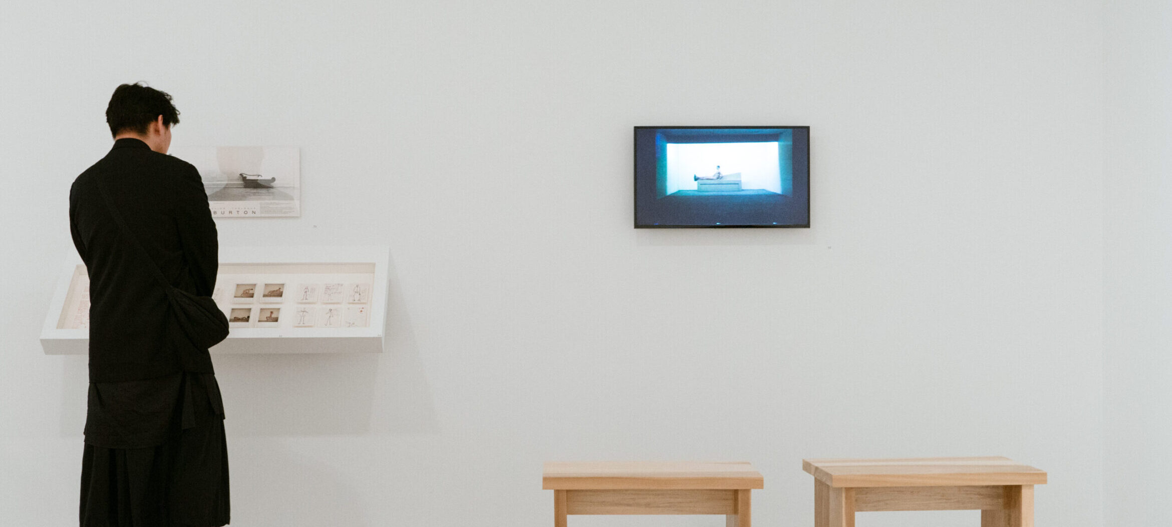 Person looking at photographs on the wall with a small tv showing an archival video.