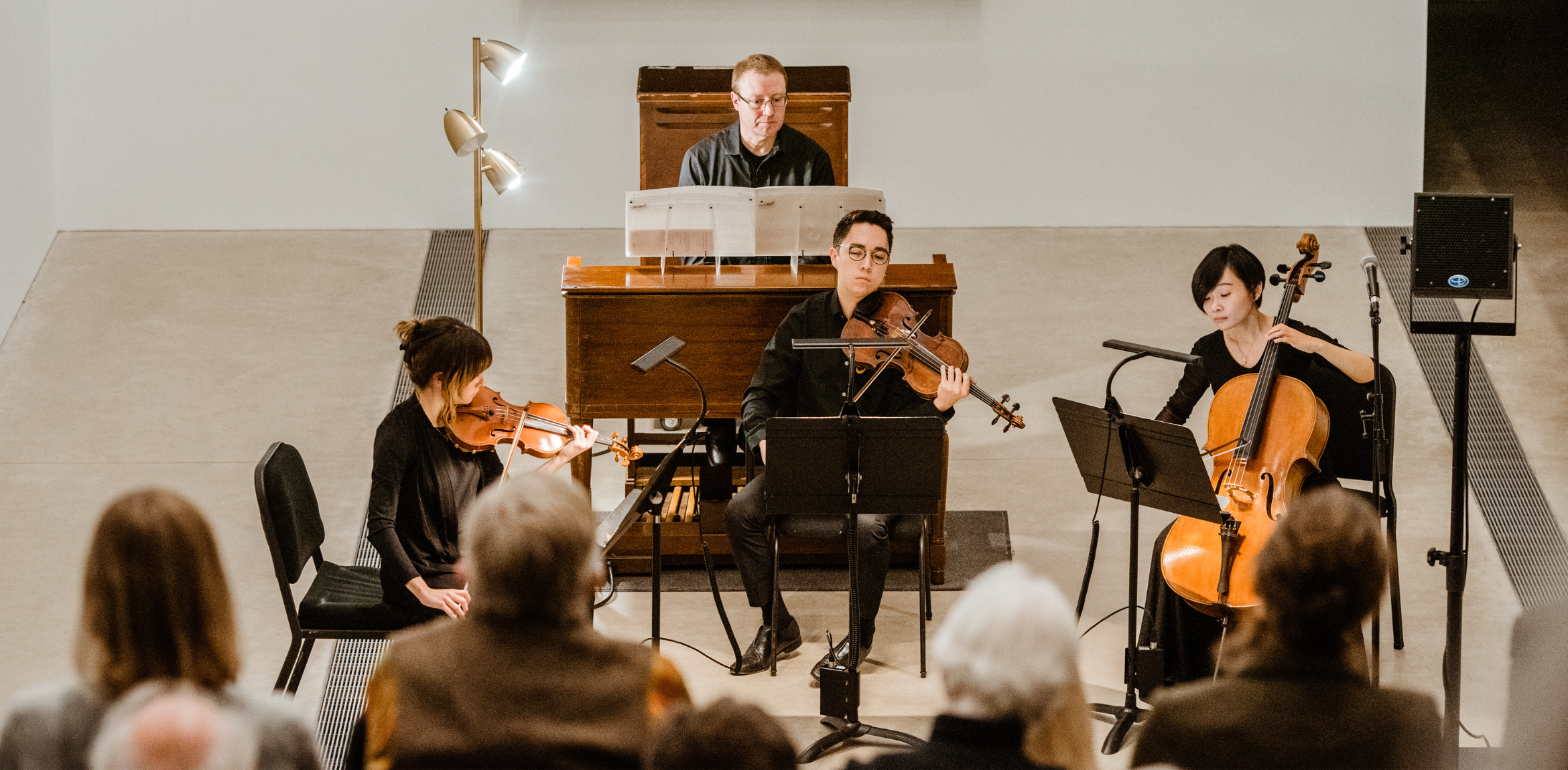 Musicians performing in an intimate setting, with a pianist, violinist, violist, and cellist captured in warm, natural lighting during a live performance.